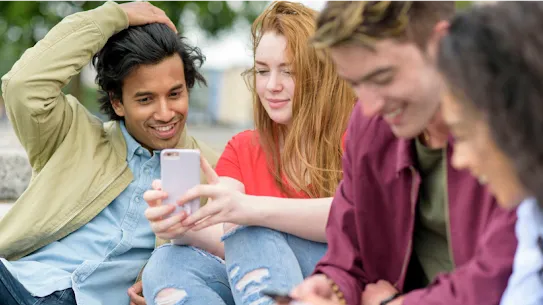 A group of smiling young people sharing information on their smartphones