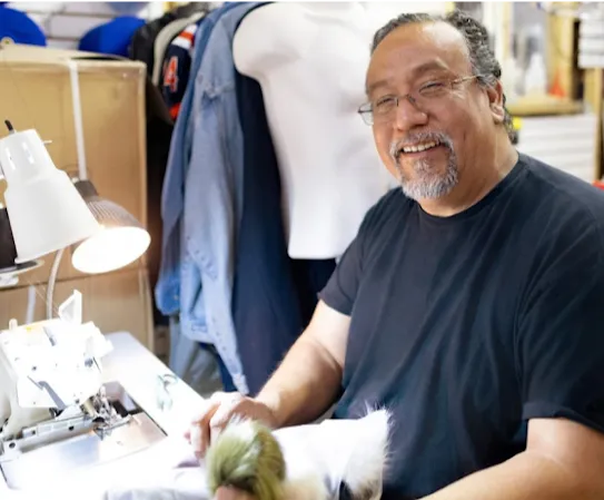 A small business owner smiles while working on his sewing machine